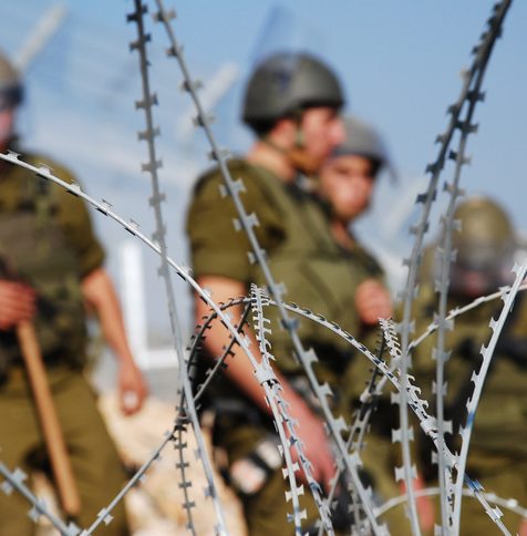 Four Israeli soldiers stand behind razor wire near the Palestinian village of Bil'in in the West Bank