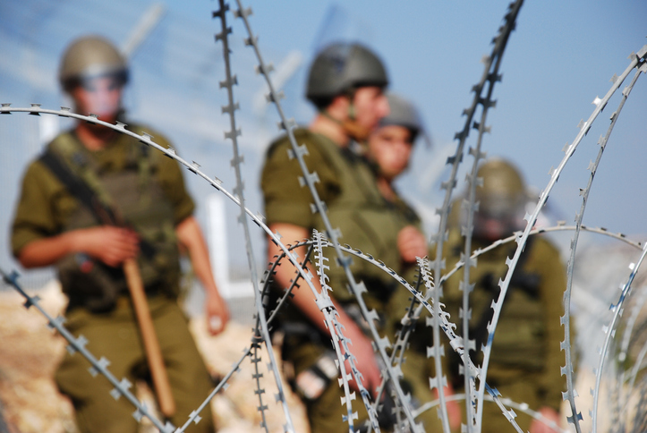 Four Israeli soldiers stand behind razor wire near the Palestinian village of Bil'in in the West Bank